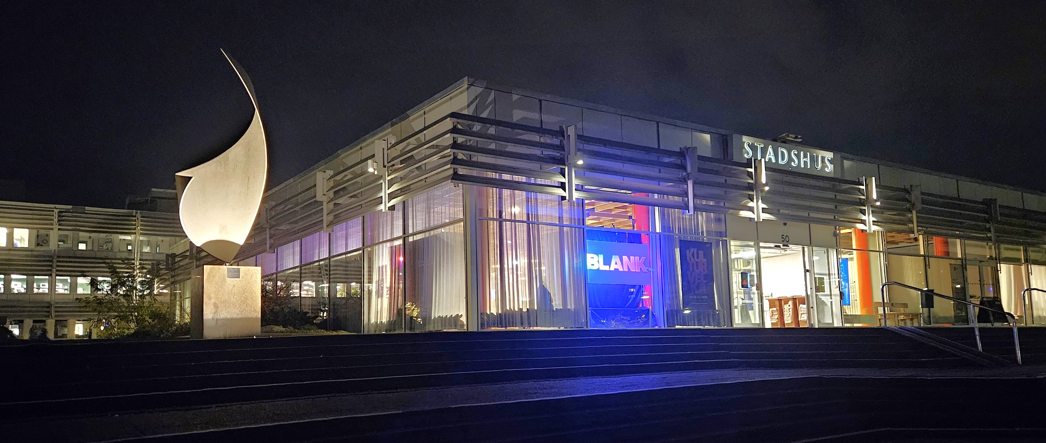 Lidingö stadshus i kvällsbelysning. Till vänster står Mi Ankarcronas "Torch of Hope" (ungefär Hoppets fackla). Inköpt 2012 av Lidingö stad. 9 november 2025.